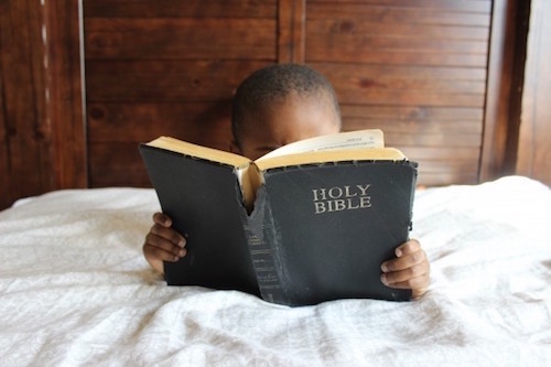 child-reading-bible-bed-african-education-boy